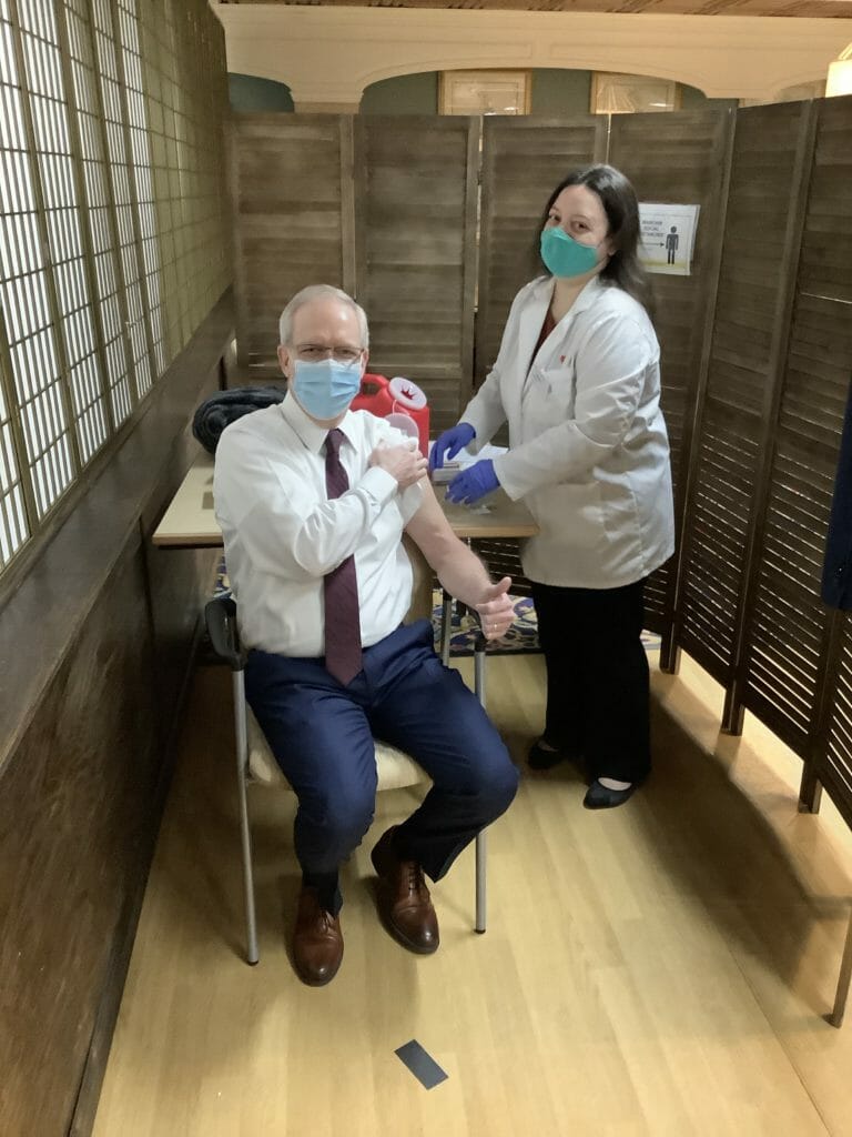 Healthcare worker giving COVID-19 vaccine to a man in a chair.