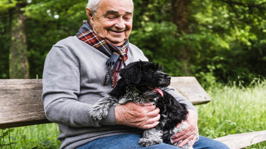 Senior wearing scarf sits outside with dog