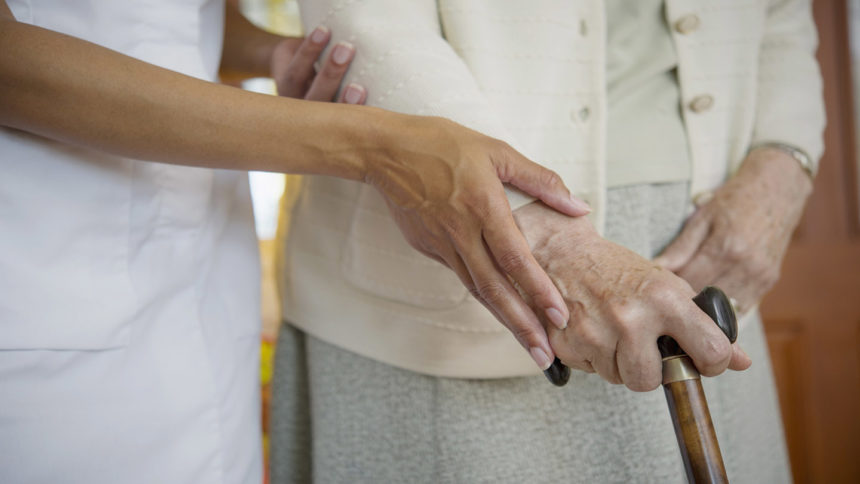 Hands of healthcare worker guiding hands of older adult on cane