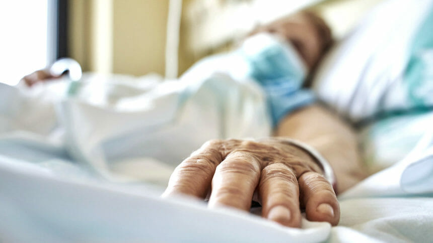 Senior woman wearing mask infected by coronavirus on hospital bed receiving medicine by drip. Close-up fingers of the senior patient ´s hand while she is sleeping. Horizontal photo