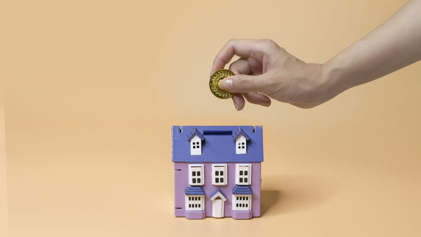 Hands inserting coin into house shape coin bank.