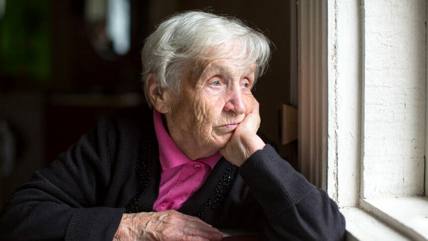 An elderly woman sadly looking out the window. Melancholy and depressed.