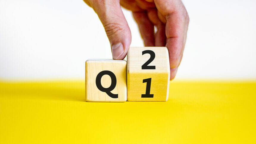 From 1st to 2nd quarter symbol. Businessman turns a wooden cube and changes words 'Q1' to 'Q2'. Beautiful yellow table, white background. Business, happy 2nd quarter Q2 concept, copy space.