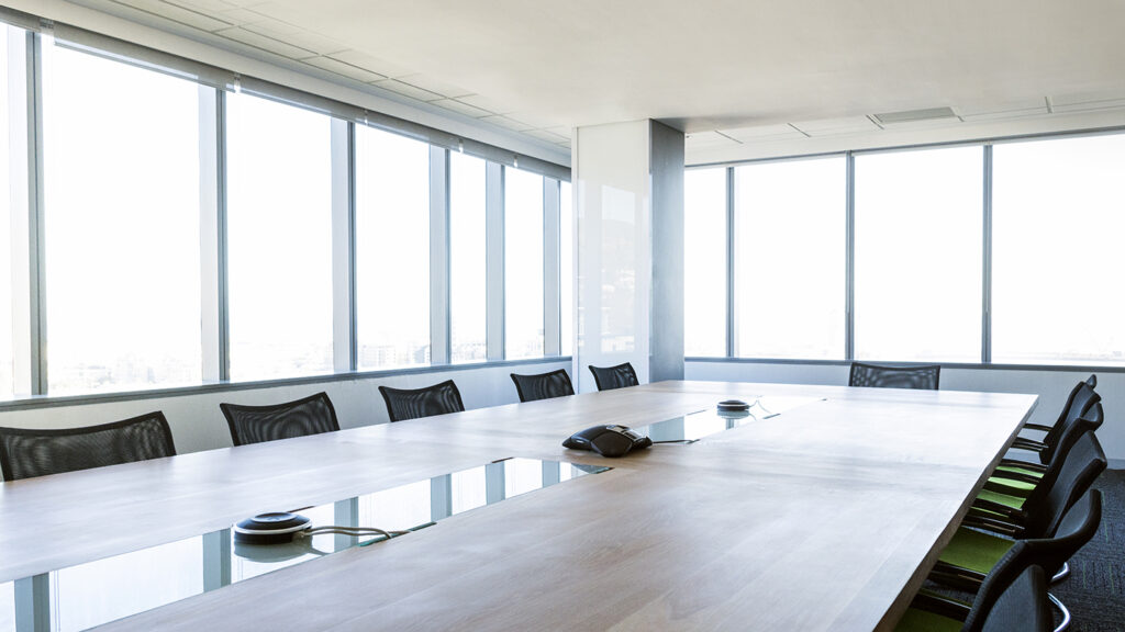 Interior of board room. Conference phone is on table. Windows are in a row at bright daylight modern office. Financial companies board of directors room.