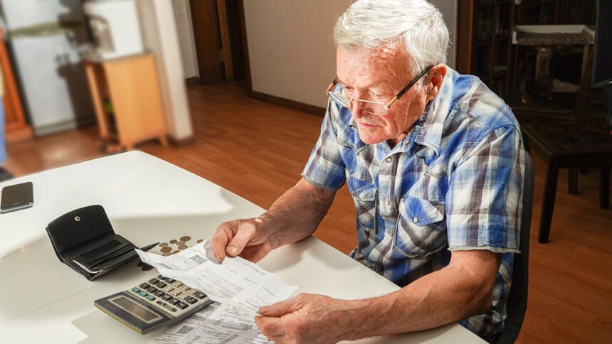 Senior man sitting at the table and calculating finances. Old man checking bills. Man counting coins on the table. Pension calculation concept