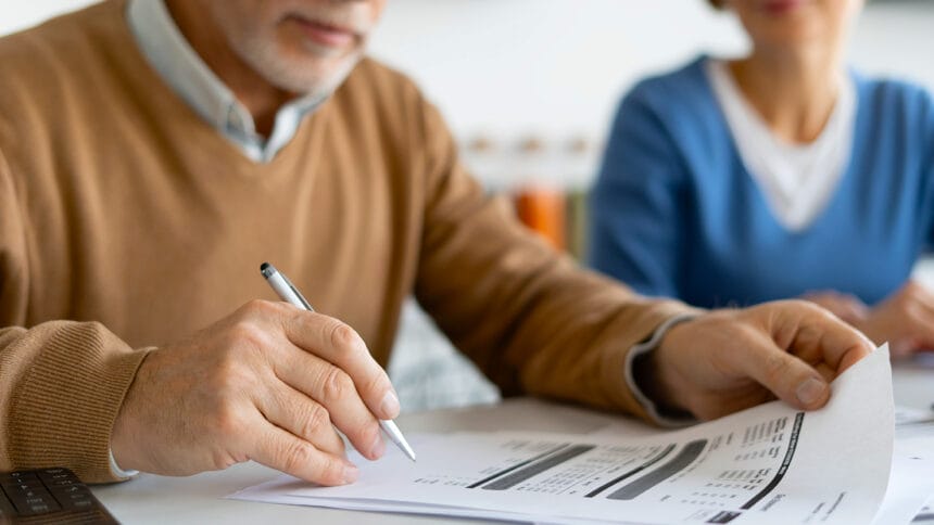 Cropped view of mature man holding pen and checking tax form or financial bill. Family couple calculate profitable investment, social benefits, pension contributions and deposits