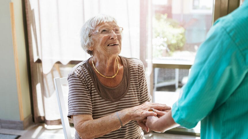 Smiling senior woman holding hands of healthcare worker at nursing home