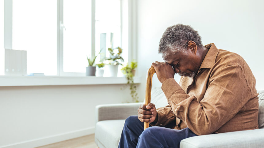 Thoughtful elderly man sitting alone at home with his walking cane