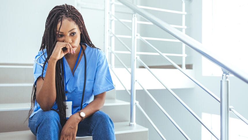 Shot of a young nurse looking stressed out while sitting at a window in a hospital. Mentally and physically exhausted. Close up of upset female nurse. Worried and stressed doctor sitting on corridor