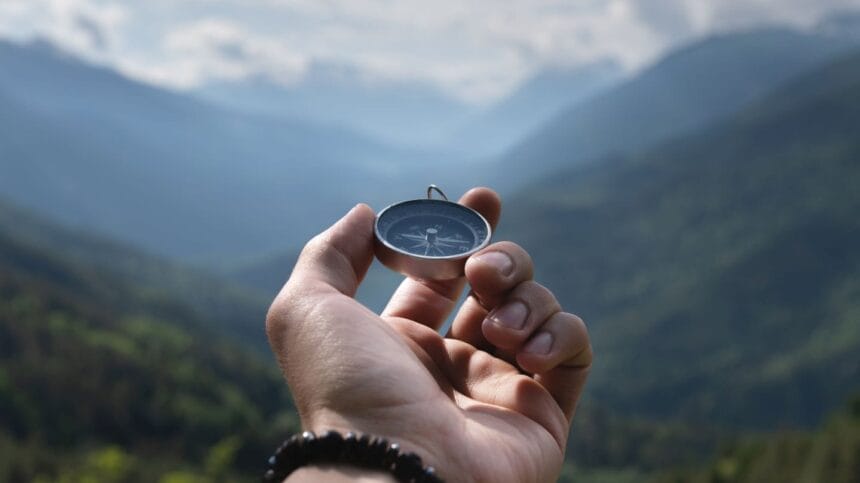 hand holding compass in front of landscape