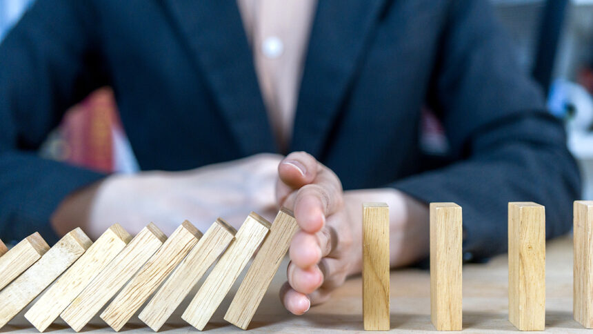 Businessman stops the domino effect. Risk management and Insurance concept.