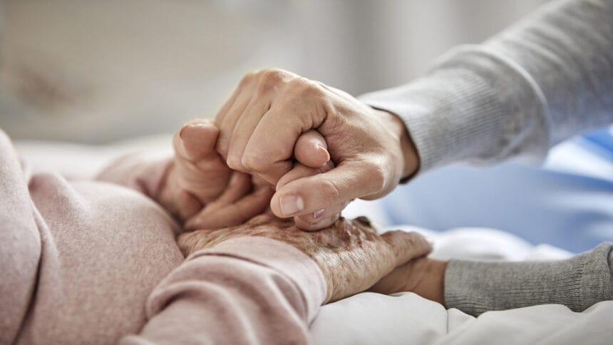 Midsection of elderly woman holding hand of nurse. Caregiver is supporting senior female. They are at home during coronavirus lockdown.