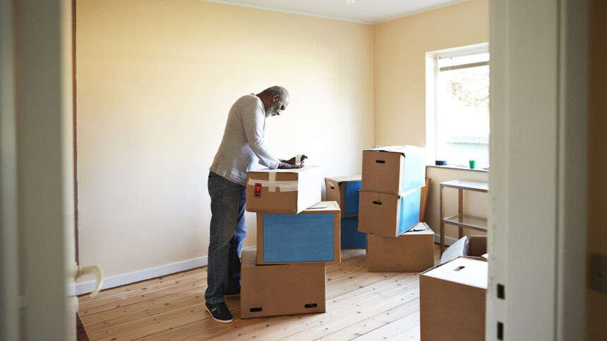 Senior Black man taping cardboard box while getting ready to relocate