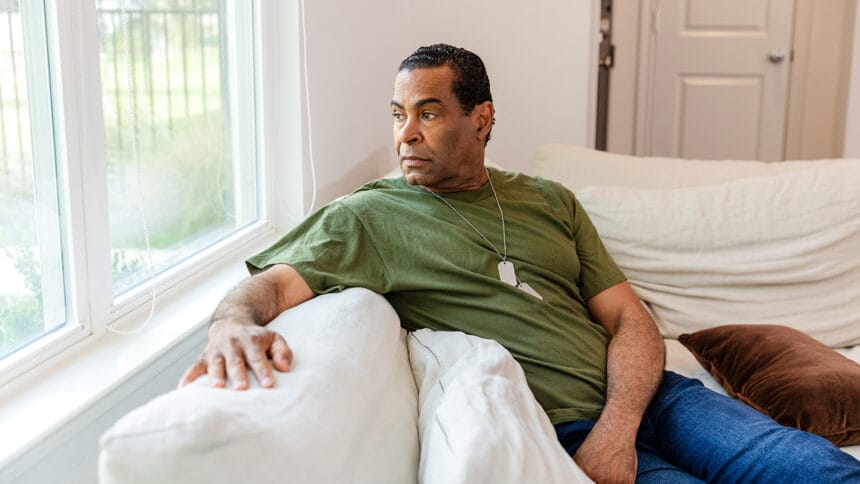 The depressed senior adult veteran deals with his PTSD alone as he sits on his sofa and looks out the window.