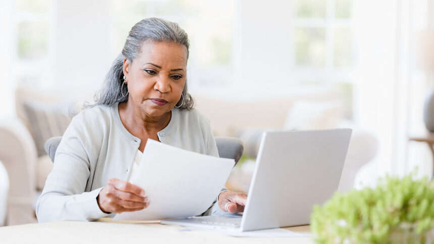 Older adult woman sitting in front of a laptop and looking at papers