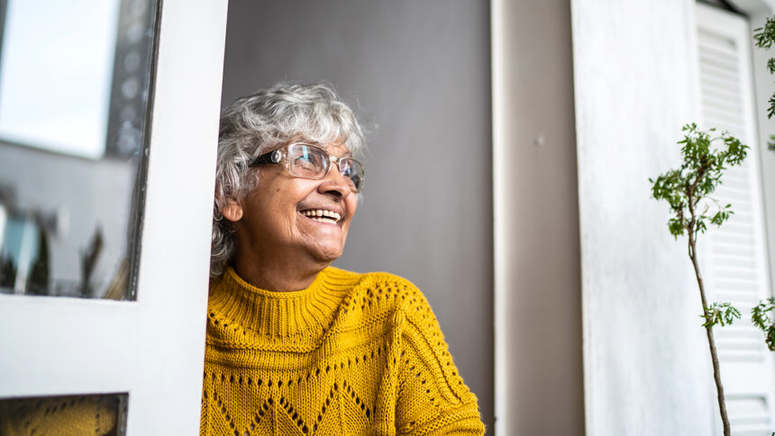 Contemplative senior woman looking through window at home