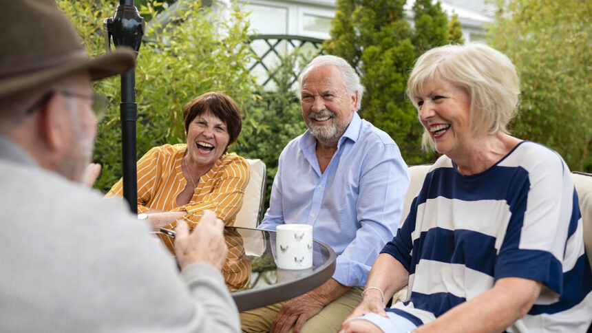 Senior friends sitting in the garden on a summers day together. They are sitting and having a laugh over a cup of tea.