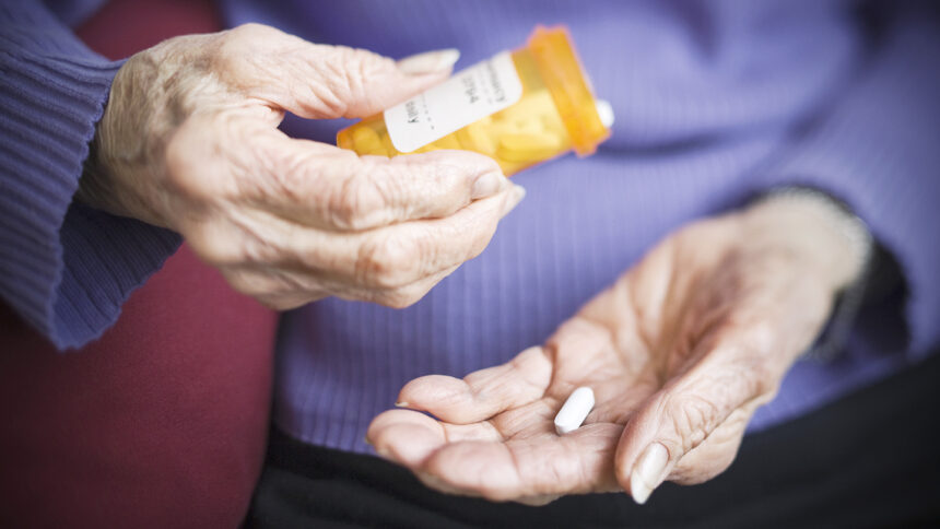 Hands of older adult woman, one holding pill bottle, the other with a pill in it