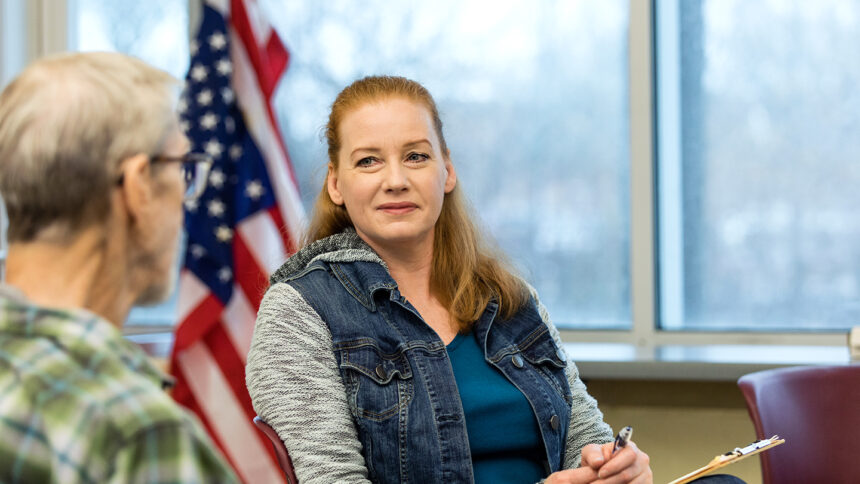 At the VA, the mature adult counselor smiles as she listens to to the unrecognizable senior adult male Vietnam veteran.