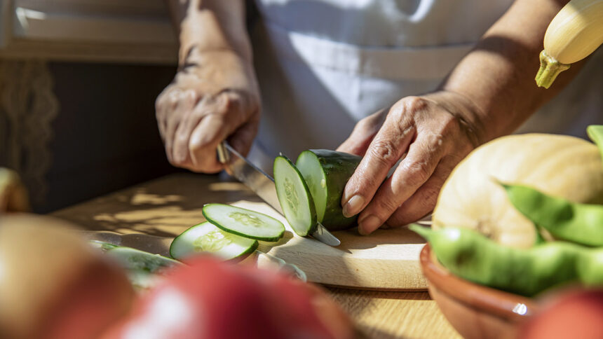 Mid section of senior Caucasian woman cutting cucumber with a knife in kitchen at home, food