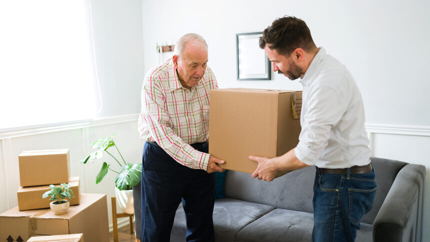 Young man carrying boxes and helping his elderly caucasian father to move to a new apartment