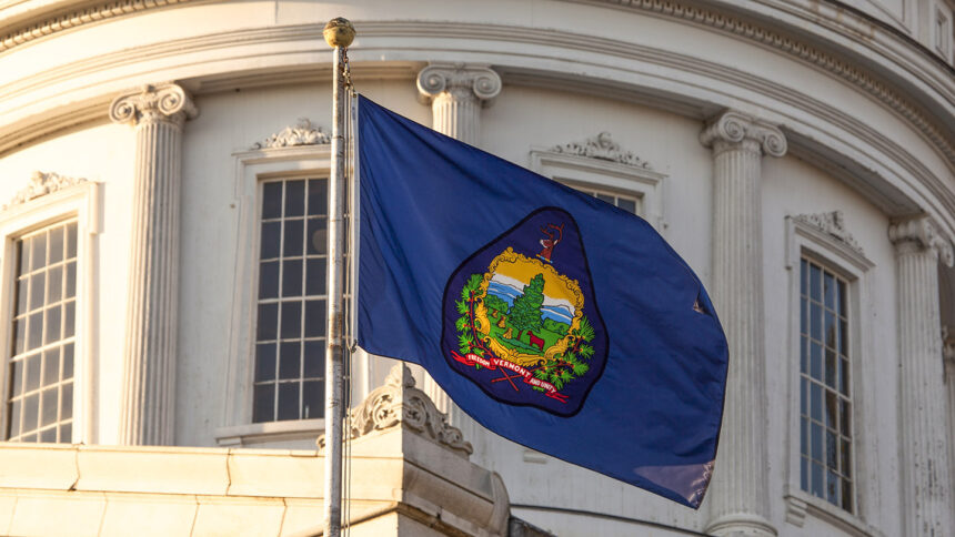 The state flag flies in front of the dome at the Vermont State House, Montpelier, VT.