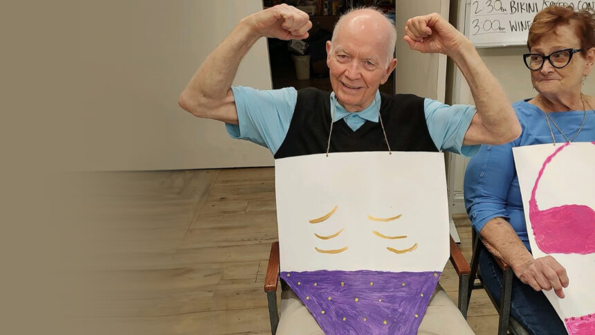 Older man with cardboard cutout of swimsuit in front of him.