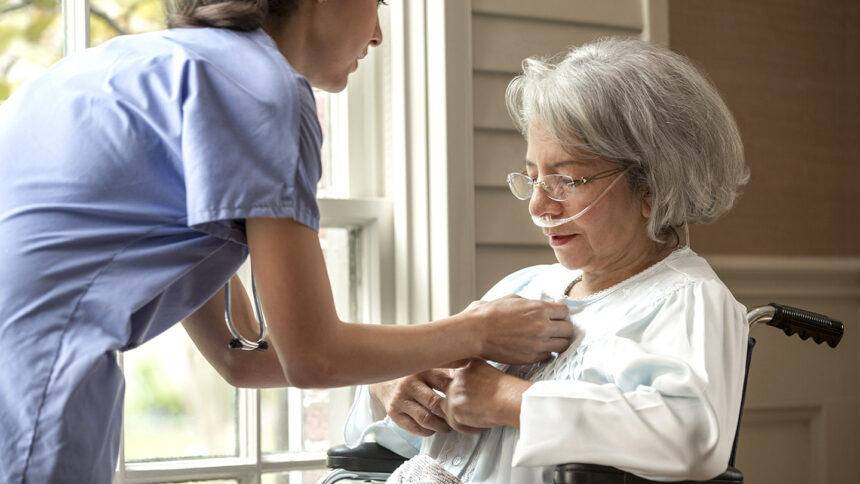 Nurse buttoning shirt of patient in wheelchair near window