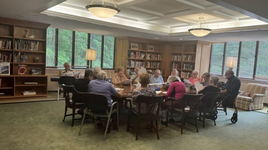 a bunch of older adults sitting around a table reading