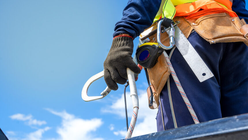 Construction worker wearing safety harness and safety line working on a metal roof.