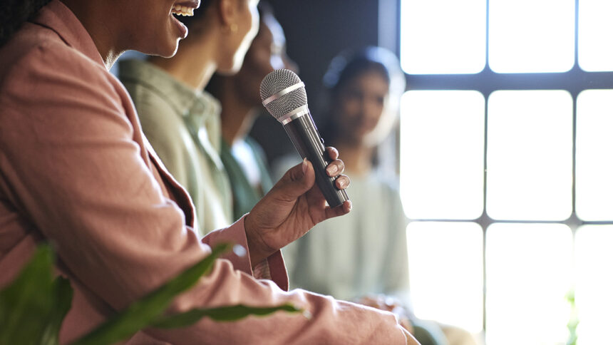 Midsection of young businesswoman explaining through microphone sitting by female colleagues in office during panel discussion