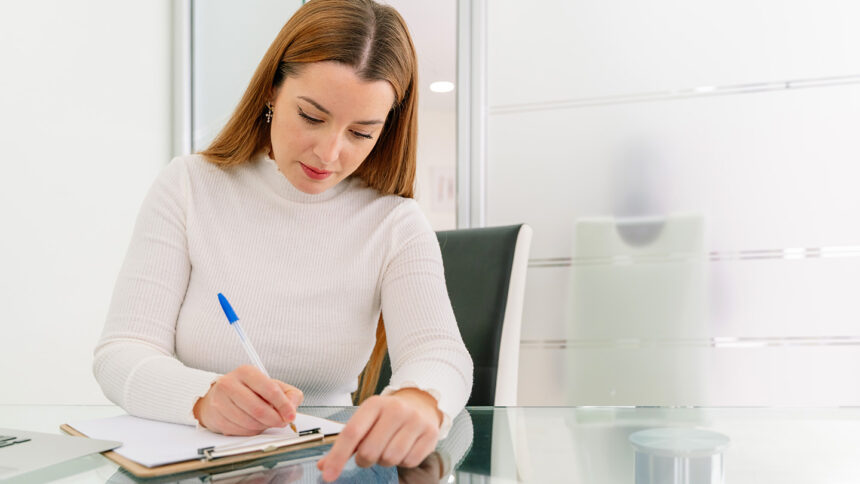 Horizontal front view of beautiful brunette woman writting with pen and paper at medical appointment. Healthcare and medical lifestyles.