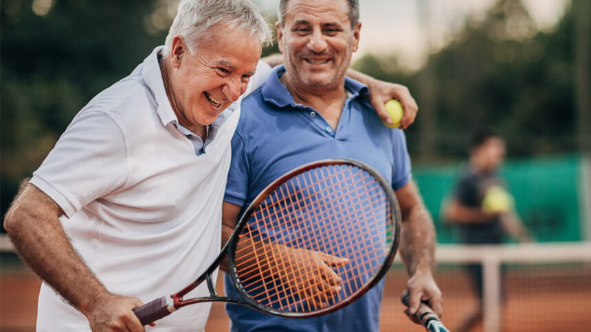 Two cheerful senior tennis players leaving tennis court after a match while smiling and hugging. Concept of healthy and fit senior people.