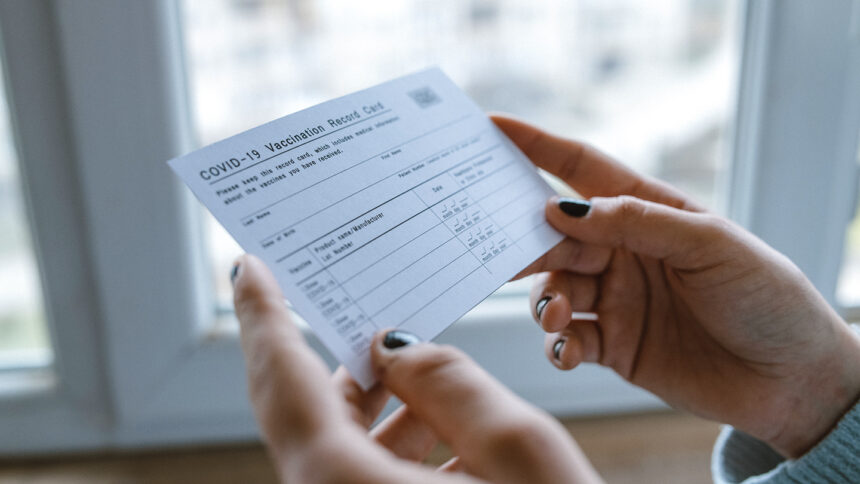 Close up of cropped female hands holding COVID-19 vaccination record card.